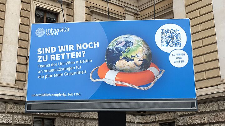 Foto vom Billboard vor dem Hauptgebäude. Blaues Sujet mit Erdball in einem Rettungsring. Folgender Schriftzug steht darauf: Planet und Mensch: Sind wir noch zu retten? Teams der Uni Wien arbeiten an neuen Lösungen für planetare Gesundheit.